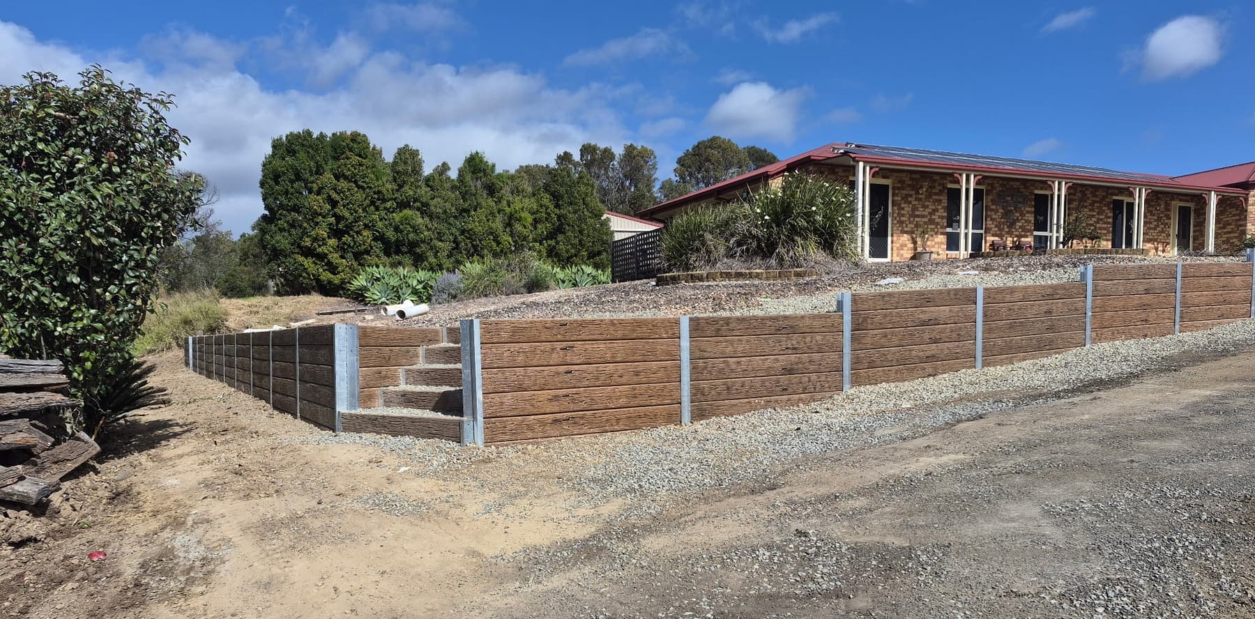 A long timber look concrete sleeper wall with steps, running along a slope on an acreage block